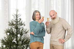 Senior couple holding champaigne glasses near a christmas tree