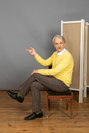 Mann sitzt auf stuhl und zeigt nach links