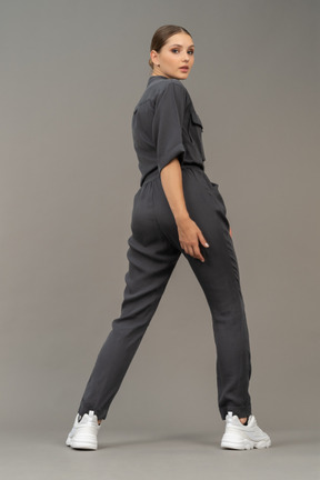 Three-quarter back view of a young woman in a jumpsuit making a step