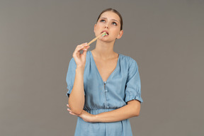 Front view of a young woman in blue dress brushing her teeth