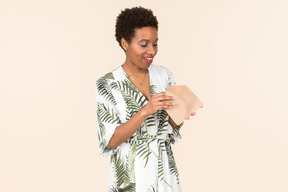 Black short-haired woman in a white and green dress, standing with an envelope in her hand