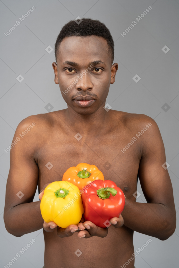 A shirtless young man holding bell peppers