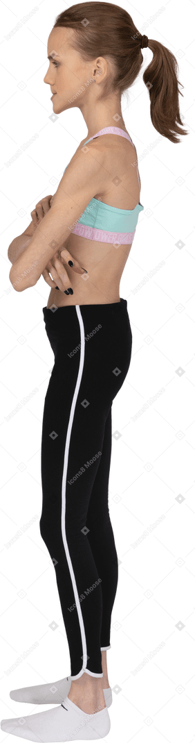 Вид сбоку девушки-подростка в спортивной одежде, скрещивающей руки и кусающей губы