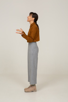 Side view of a delighted young asian female in breeches and blouse raising hands