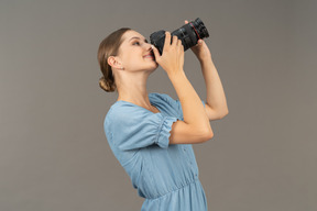 Three-quarter view of a smiling young woman in blue dress taking shot