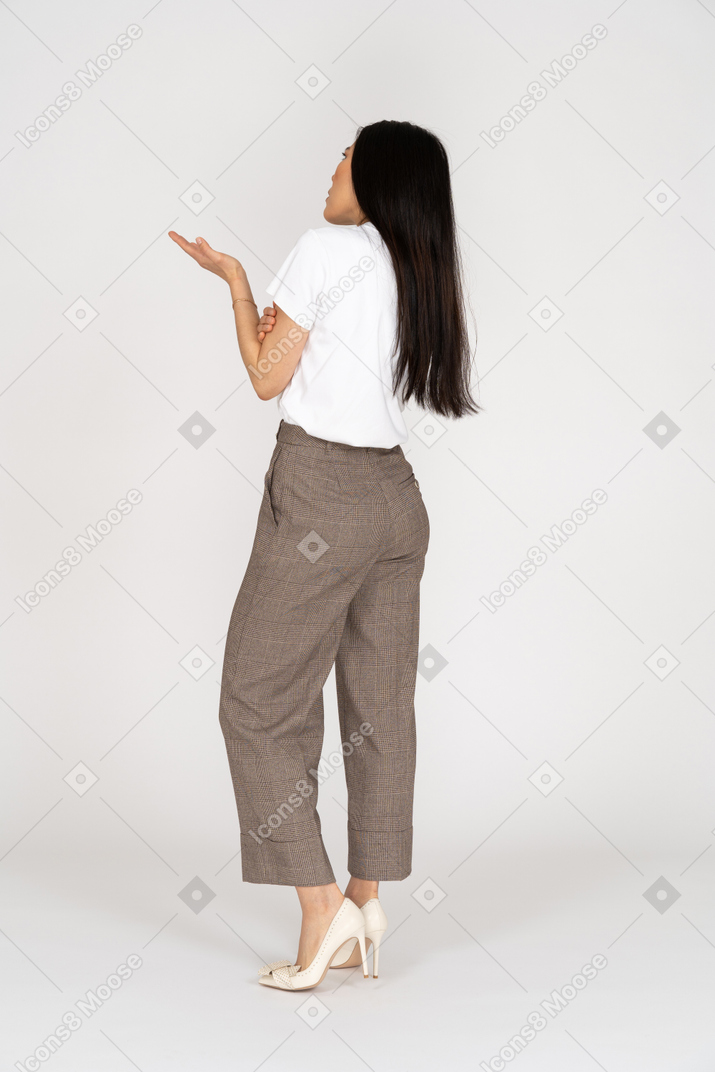 Vista traseira de três quartos de uma jovem maravilhada de calça e camiseta levantando a mão