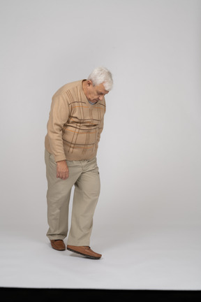Front view of an old man in casual clothes walking and looking down