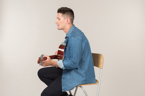 Young guy sitting on the table in profile and playing on guitar
