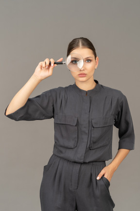 Front view of a young woman in a jumpsuit holding a magnifying glass