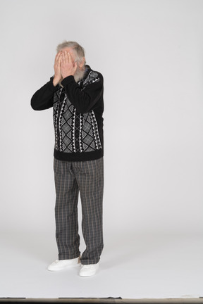 Elderly man facing the camera and covering his face with his hands