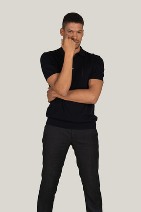 Pensive young man in black pants and t-shirt closing face with the hand