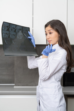 困惑的女医生拿着x射线图像并在旁边看的侧视图