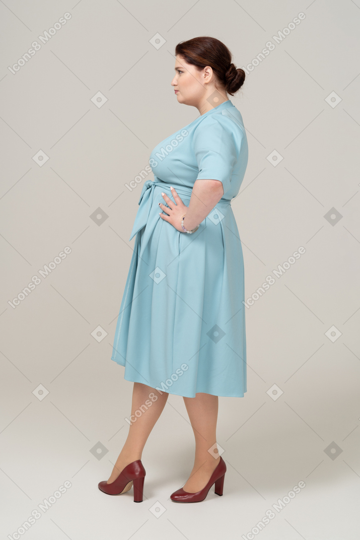 엉덩이에 손을 대고 포즈를 취하는 파란 드레스를 입은 여자의 측면보기
