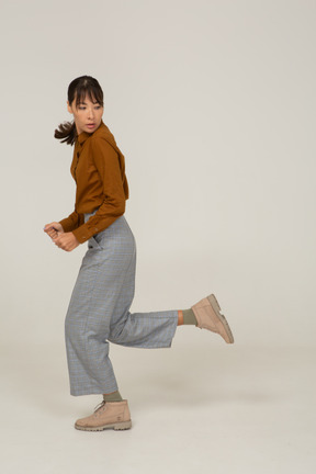 Vista lateral de una joven mujer asiática corriendo en calzones y blusa alejándose