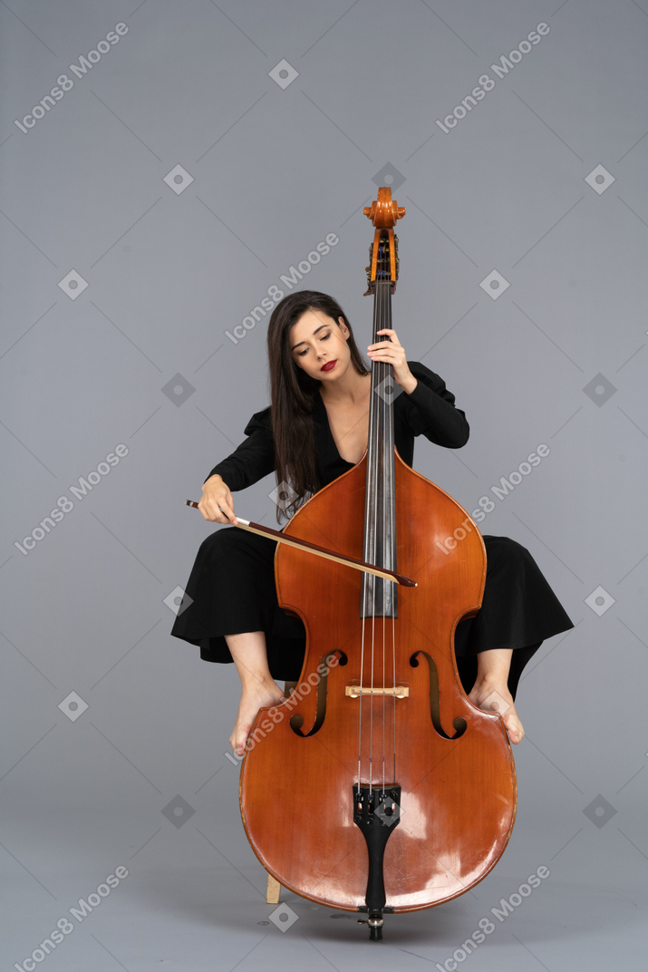Vorderansicht einer jungen dame, die auf einem stuhl sitzt, während beine auf kontrabass setzen