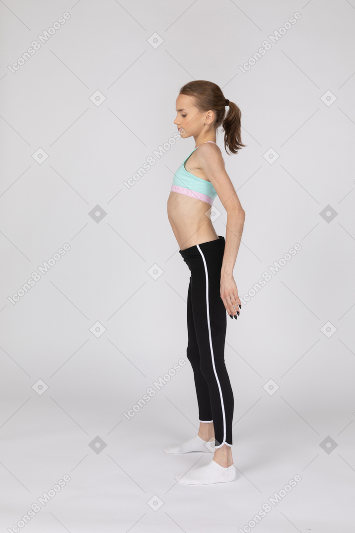 Vista lateral de una jovencita en ropa deportiva estirando su espalda y mirando hacia abajo