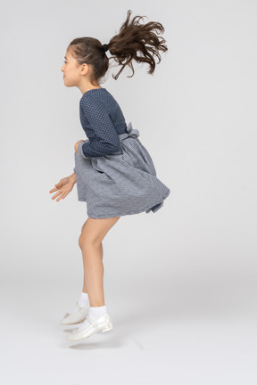 Side view of a girl jumping while holding the hem of the skirt