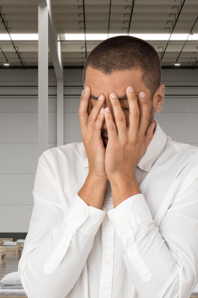 A man in a white shirt covering his eyes