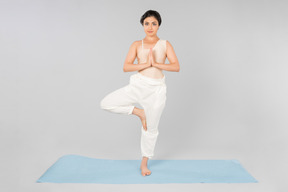 Junge indische frau, die in baumstellung auf yogamatte steht
