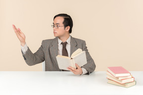 An asian teacher in a checkered suit, a tie and a book in his hand, working with the class