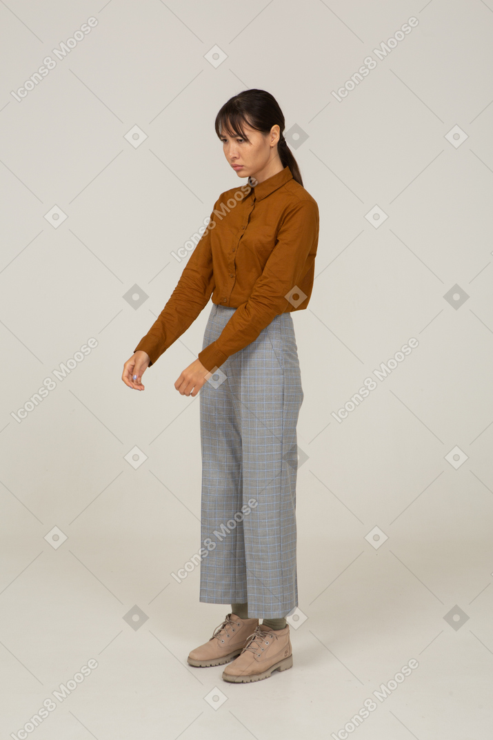 Vista di tre quarti di una giovane donna asiatica in calzoni e camicetta che allunga le mani
