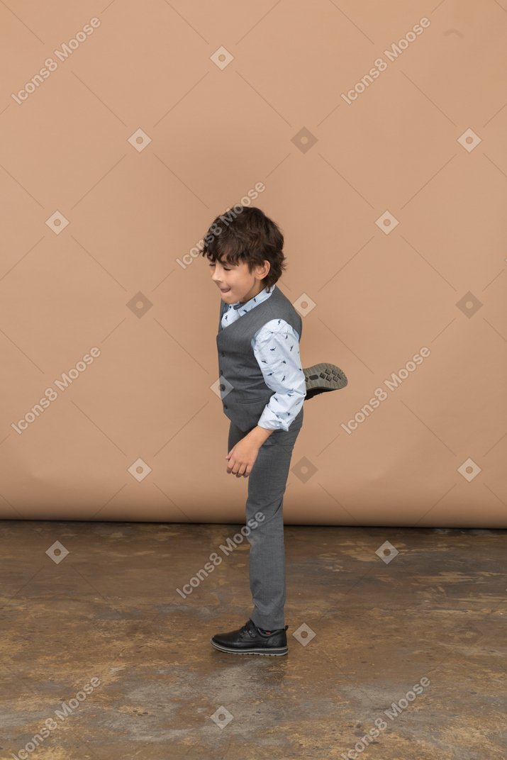 Vista lateral de um menino de terno cinza posando em uma perna