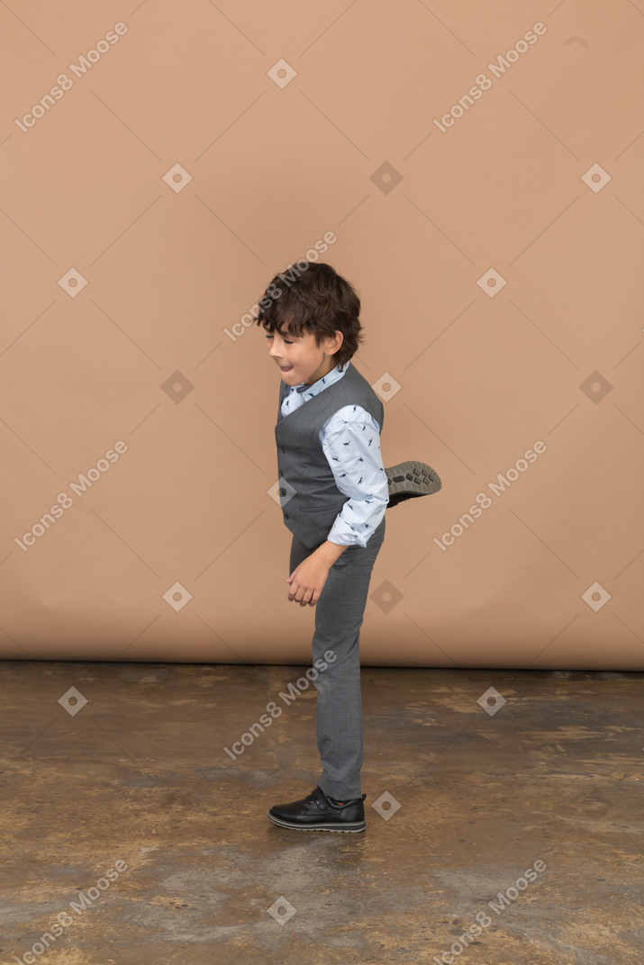 Side view of a boy in grey suit posing on one leg