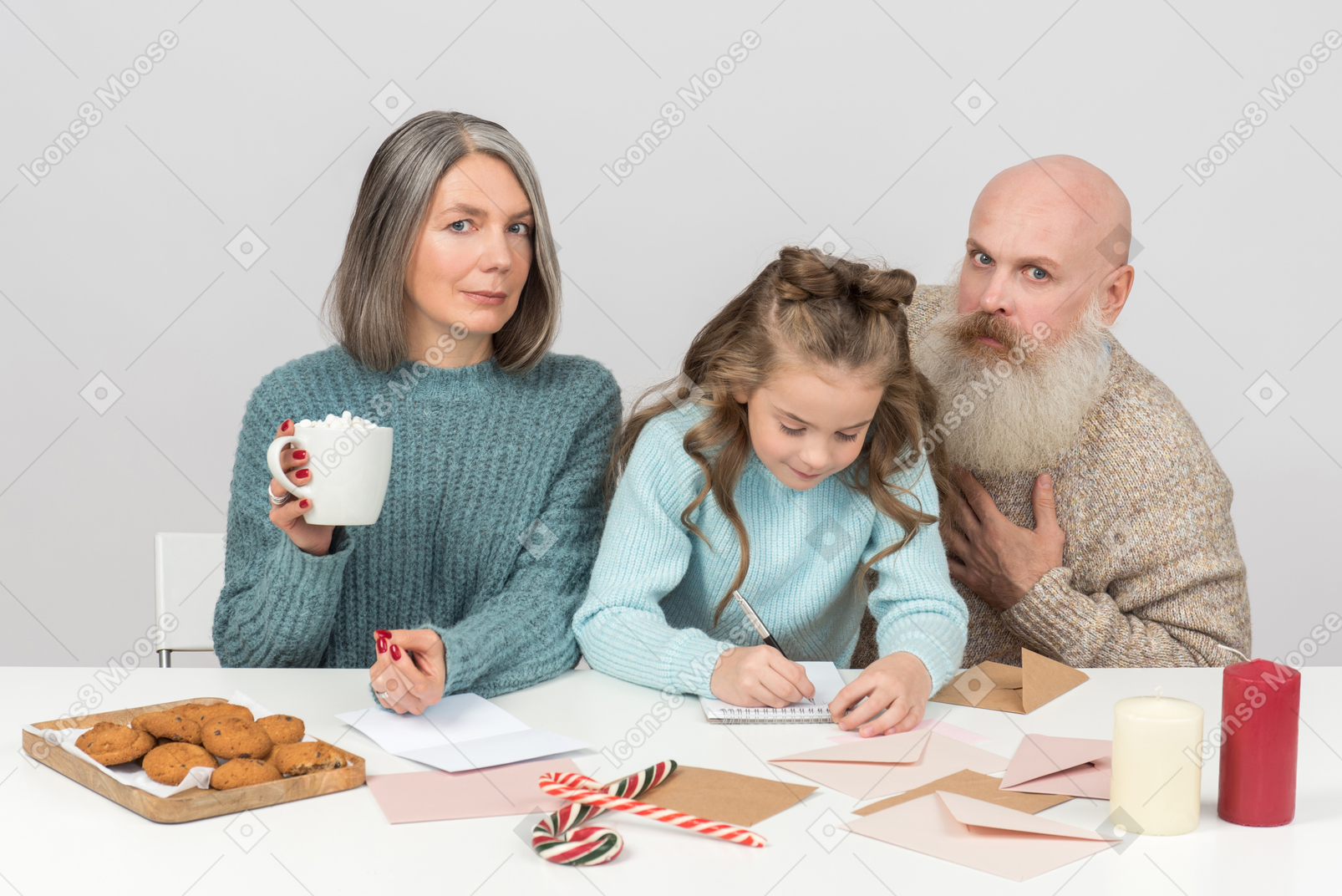 Grandparents and granddaughter having cacao with cookies and signing postcards