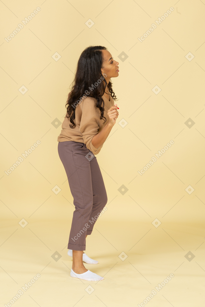 Vista lateral de una mujer joven de piel oscura bailando levantando las manos