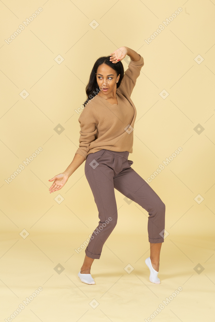 Three-quarter view of a dark-skinned dancing young female raising hand while looking aside