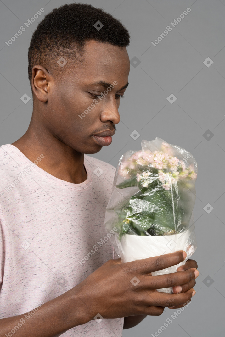 Young man holding flower pot covered with plastic