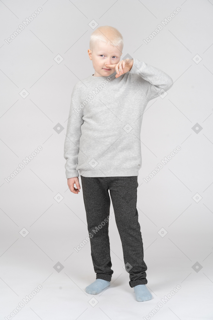 Вид спереди морщинистого мальчика, касающегося носа и смотрящего в сторону