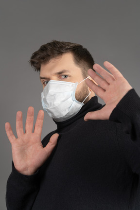 Scared brunette man in medical mask making a stop hand sign