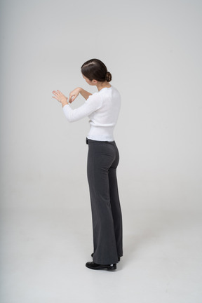 Vue latérale d'une femme en pantalon noir et chemisier blanc regardant sa main