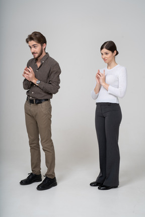 Three-quarter view of a sly young couple in office clothing holding hands together