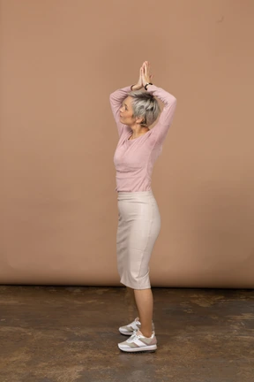 Side view of a woman in casual clothes posing with hands above head