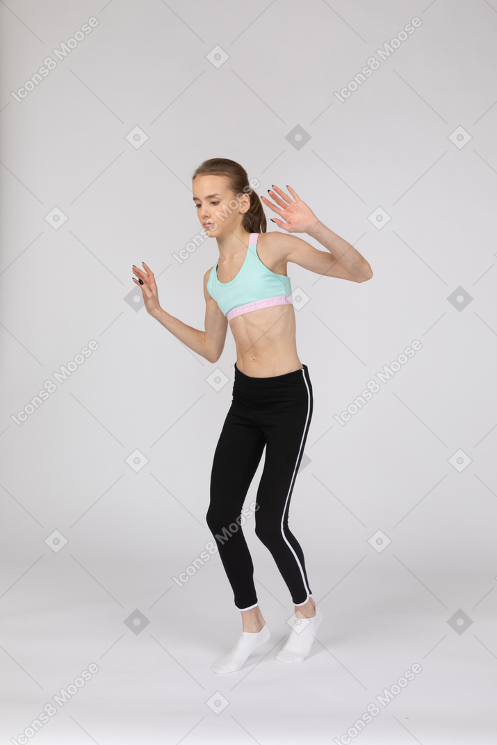 Vista de tres cuartos de una jovencita en ropa deportiva caminando cautelosamente de puntillas