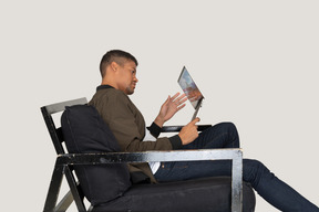 Side view of young man sitting on a sofa and holding a laptop