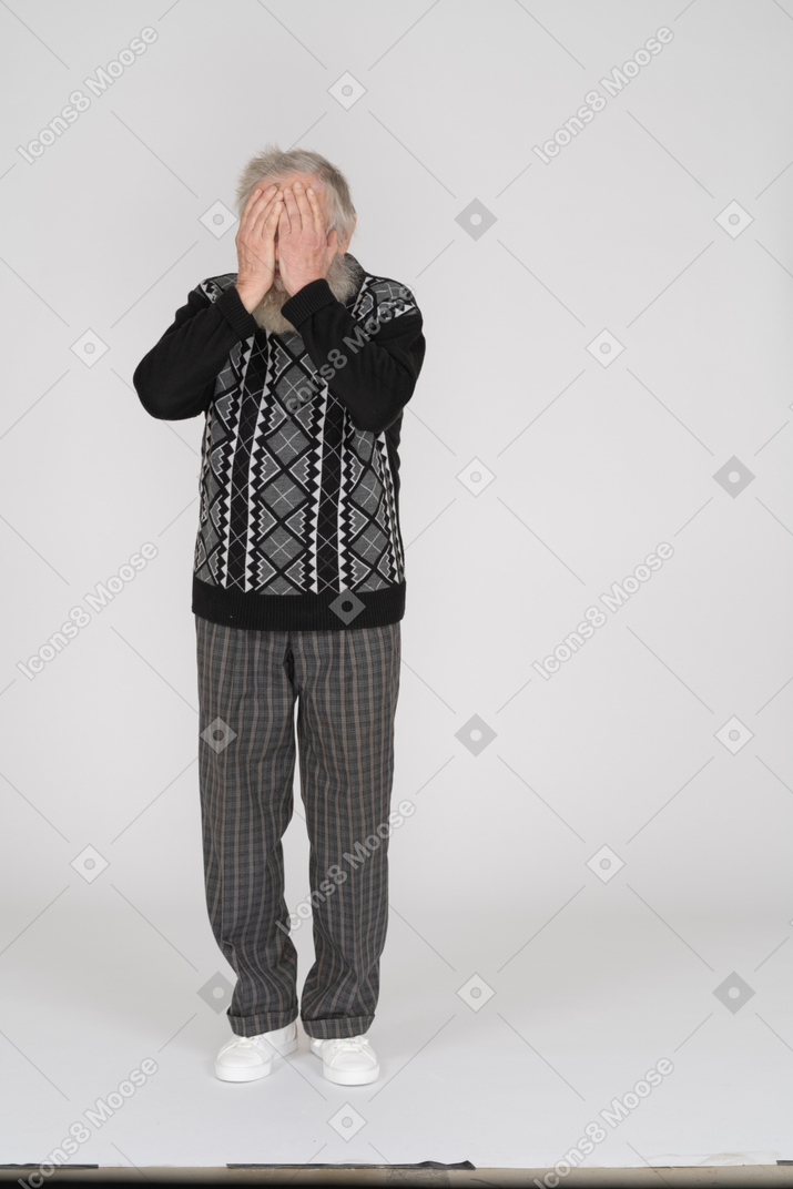 Älterer mann, der die kamera gegenüberstellt und sein gesicht mit seinen händen bedeckt