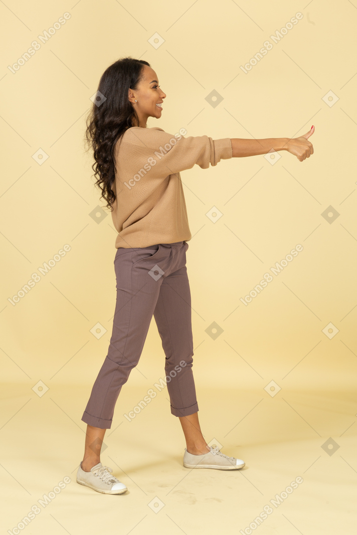 Вид сбоку довольной темнокожей молодой женщины, показывающей большой палец вверх