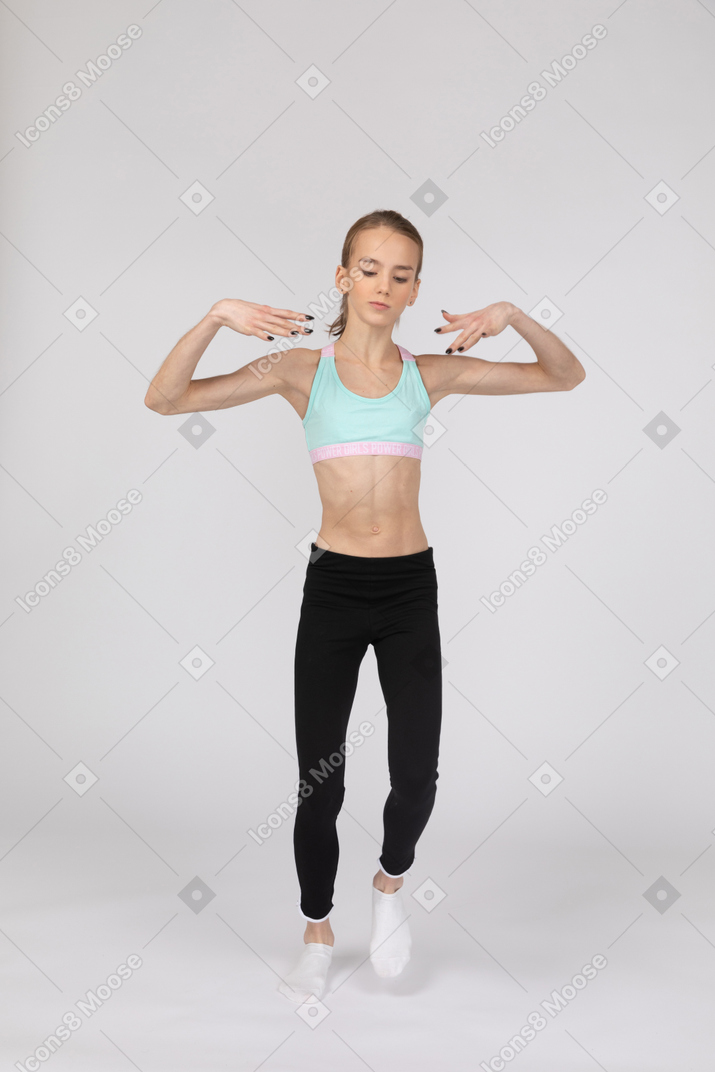 Vista frontal de uma adolescente em roupas esportivas, levantando ambas as mãos enquanto dança