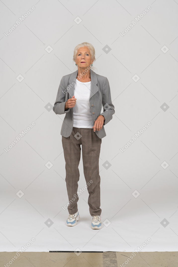 Front view of an impressed old lady in suit standing on toes