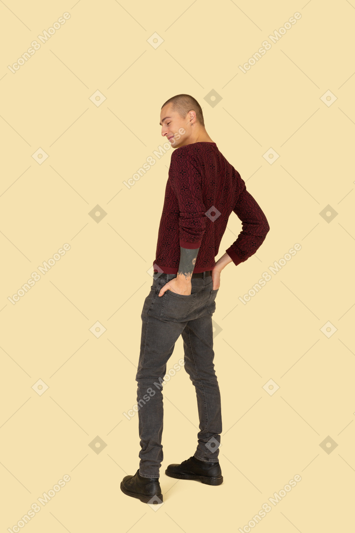 Three-quarter view of a young man in red pullover putting hands in back pockets