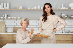 A woman with tray of cookies standing next to a woman with cookie in hand