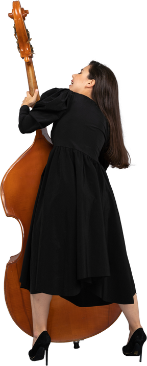 Vista posteriore di una giovane musicista in abito nero che tiene il suo contrabbasso