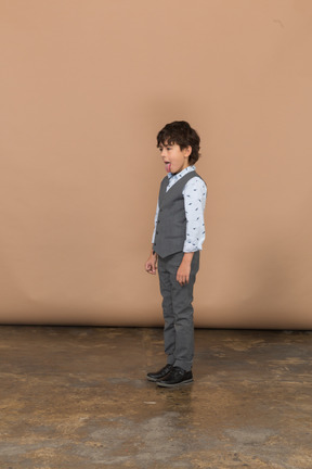 Vista lateral de um menino de terno cinza mostrando a língua