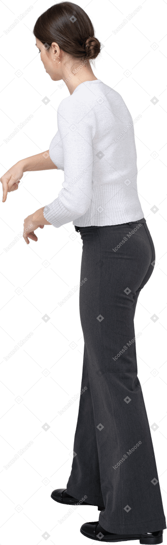 Vista lateral de una mujer joven en ropa casual apuntando hacia abajo con un dedo