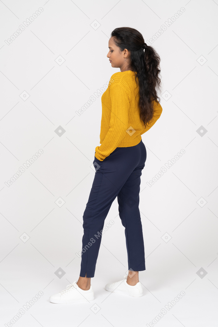 Vista lateral de uma garota com roupas casuais, posando com as mãos nos bolsos