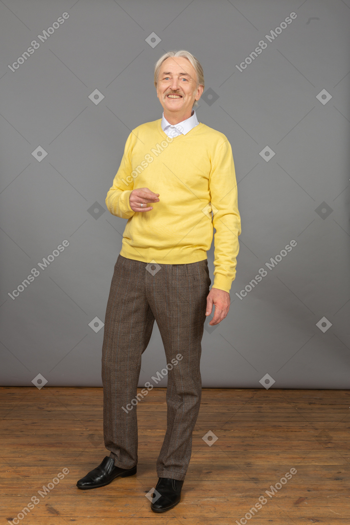 Vorderansicht eines gestikulierenden alten mannes, der gelben pullover trägt und kamera beim lächeln betrachtet
