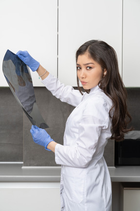 Side view of a young female doctor holding an x-ray image and looking at camera